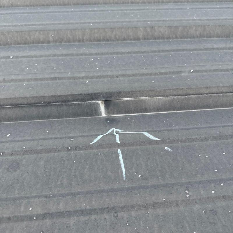 Metal roofing panel with hail damage marked for repair