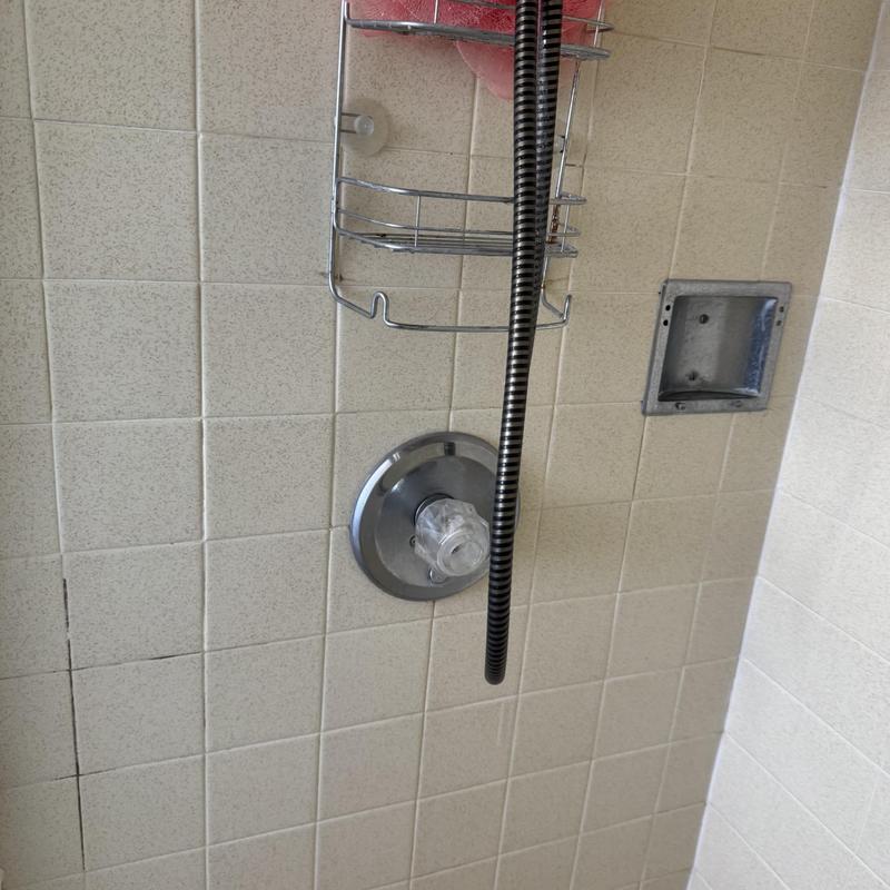 Shower valve with hose and tiled wall in bathroom