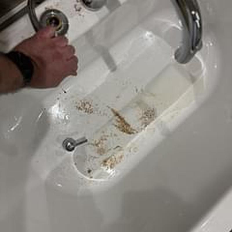 Shower drain with debris being cleared by hand