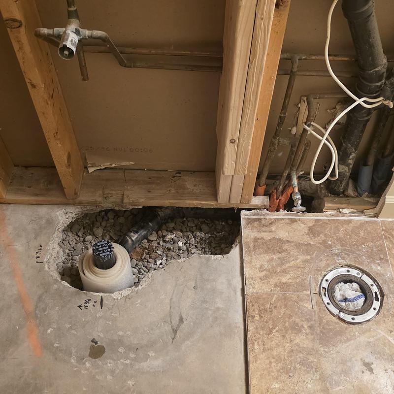 Shower drain installation with exposed plumbing and concrete floor