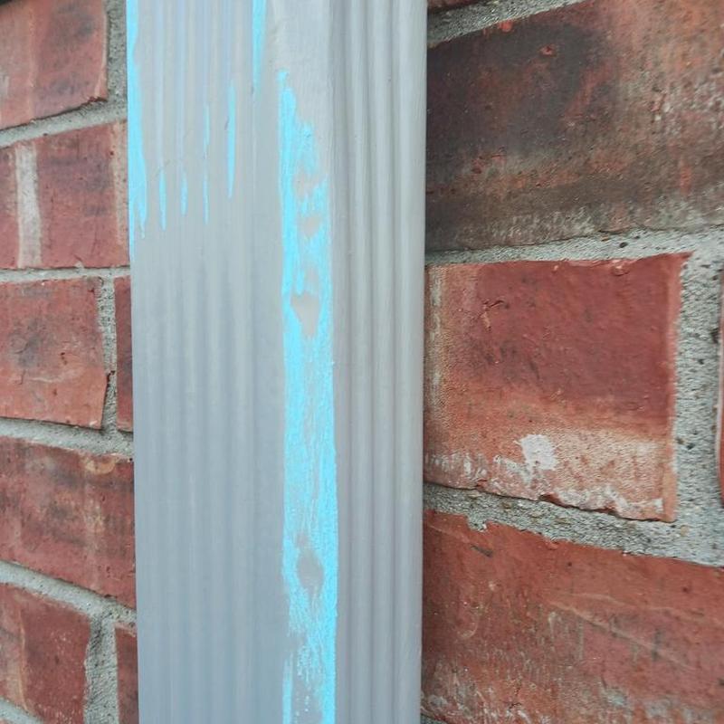 Seamless gutter downspout installation on brick wall