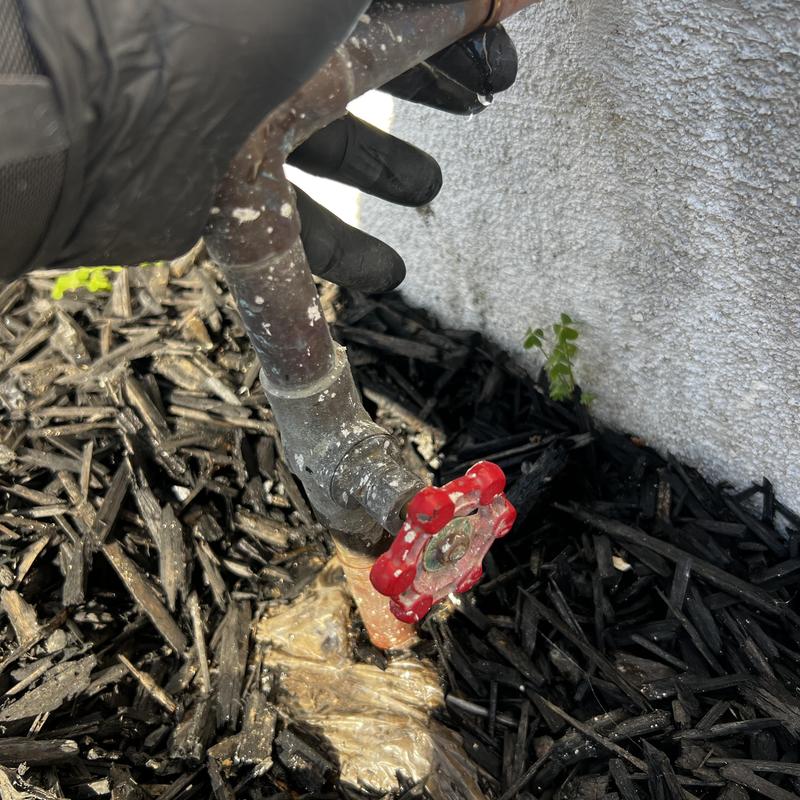 Copper water line with red valve handle near wall