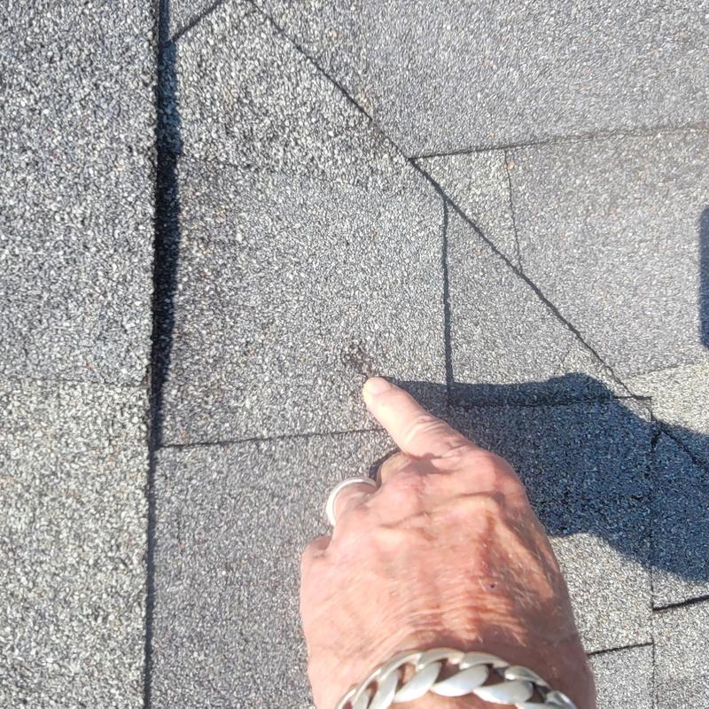 Asphalt roof shingle with hail damage being pointed at