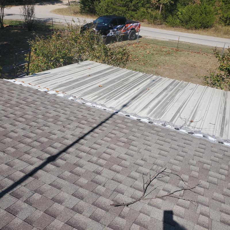 Metal roof panel with hail damage next to shingle roof