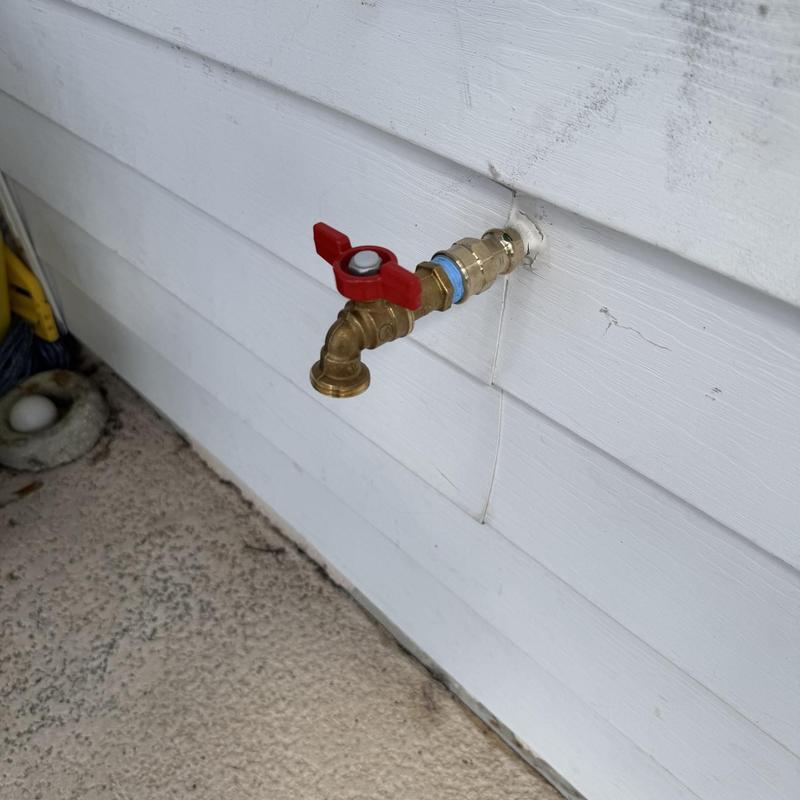 Copper hose bib with red ball valve on house exterior