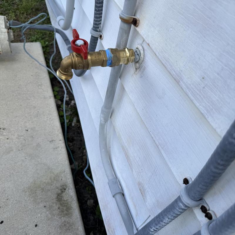 Copper hose bib with red valve on house exterior