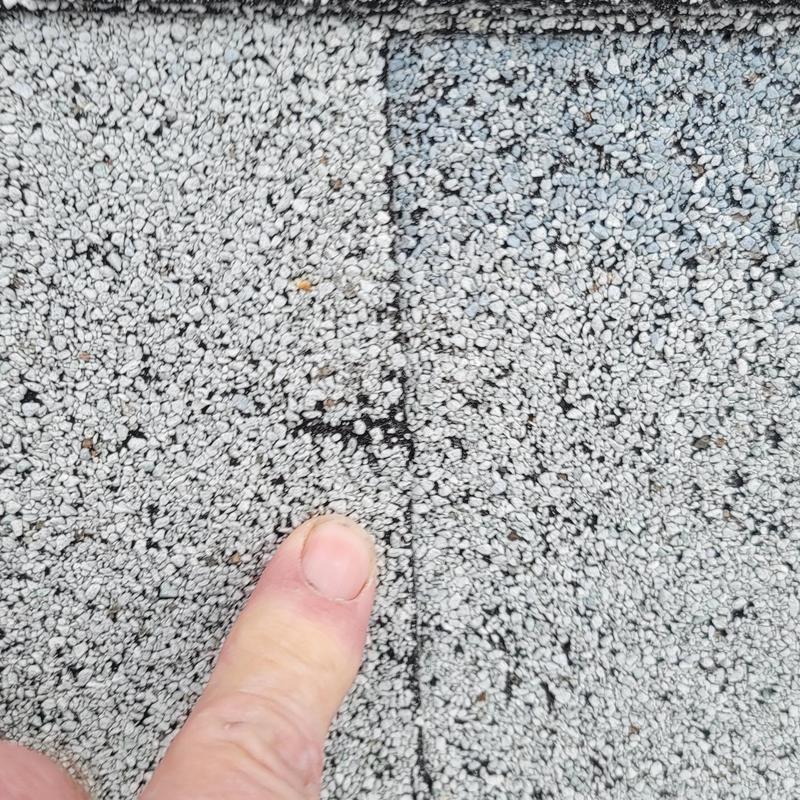 Roof shingle hail damage close-up with finger for scale