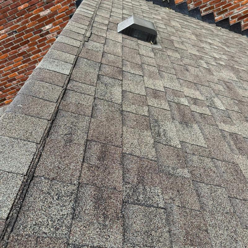 Asphalt shingle roof with metal vent and brick wall