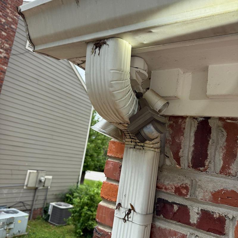 Downspout with rust and debris on brick wall corner