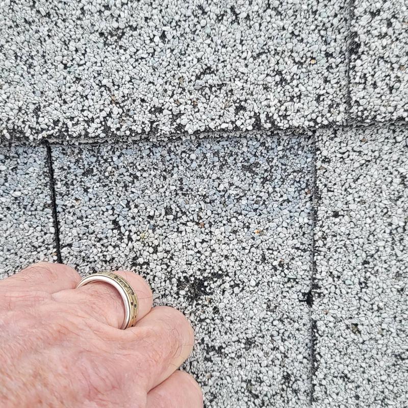 Roof shingles showing hail damage close-up with hand for scale