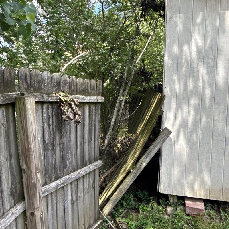 Wooden fence panel leaning against shed post with damage