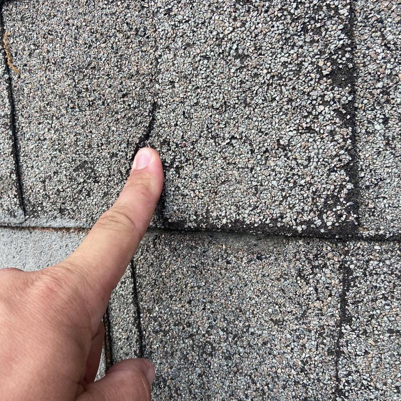Asphalt shingle with crack being inspected for leaks