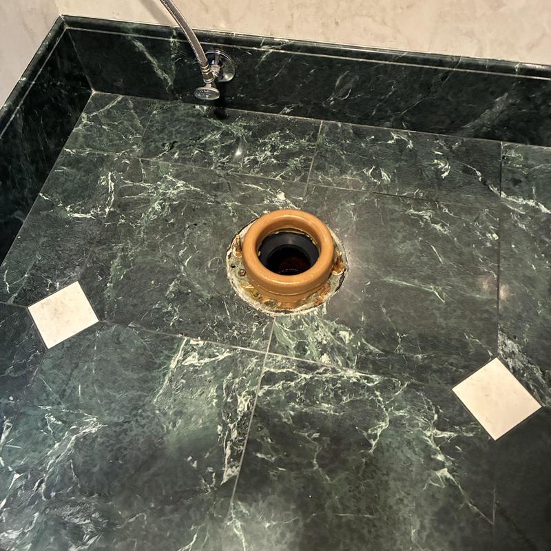 Toilet flange on dark marble floor with water supply line
