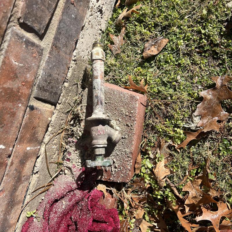 Outdoor spigot with corrosion on ground near brick wall