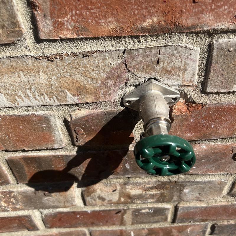 Outdoor water spigot with green handle on brick wall