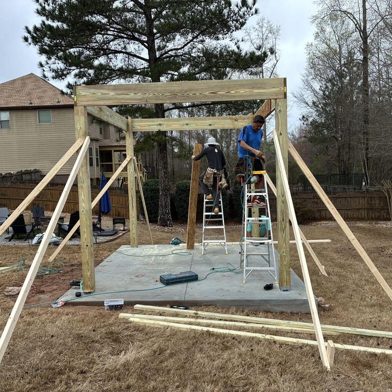 Wooden gazebo frame on concrete foundation with workers