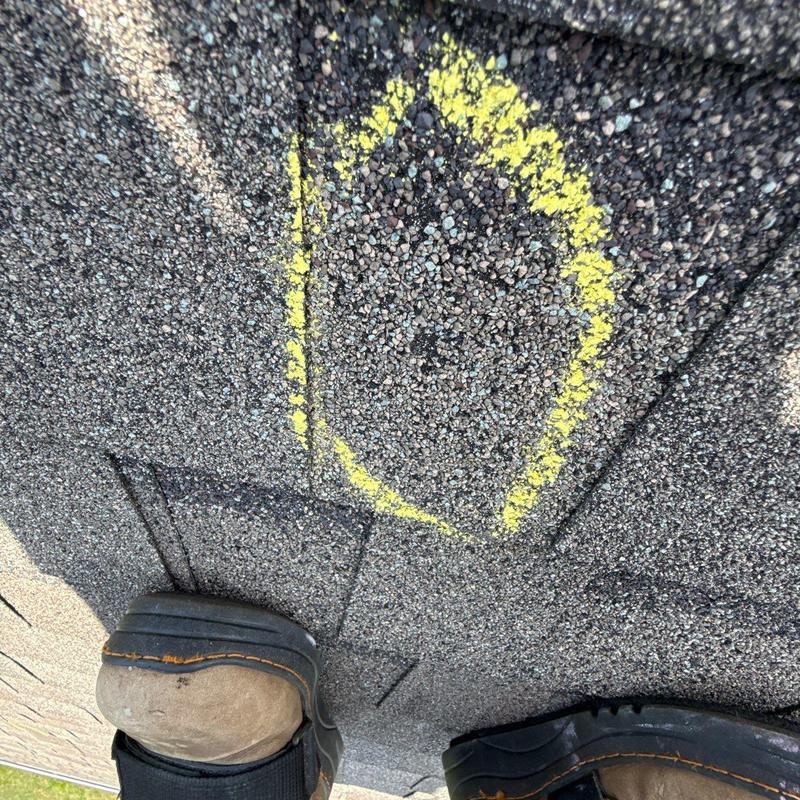 Asphalt roof shingle with yellow chalk marking on hail damage