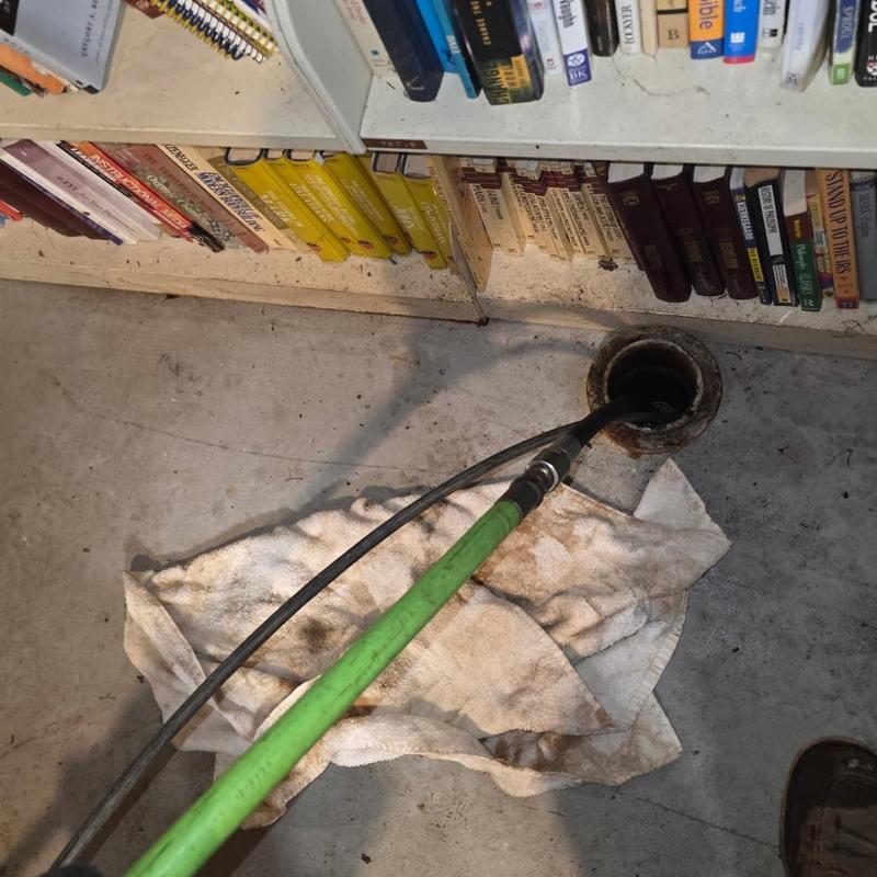 Sewer cleanout hydro jetting with green hose near bookshelf