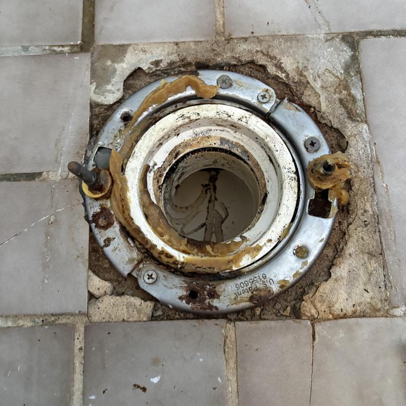 Toilet flange with old wax ring and tile floor damage