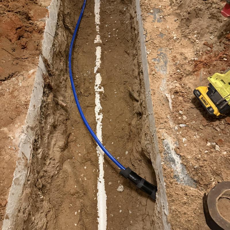 Sewer pipe with blue conduit inside trench at slab home