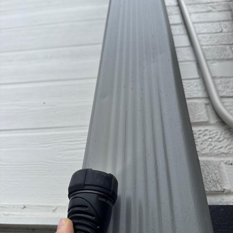 Downspout inspection with flashlight at siding wall