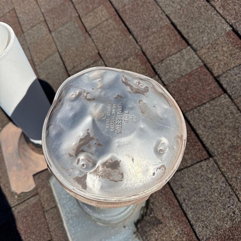 Metal roof vent cap with hail damage on shingle roof