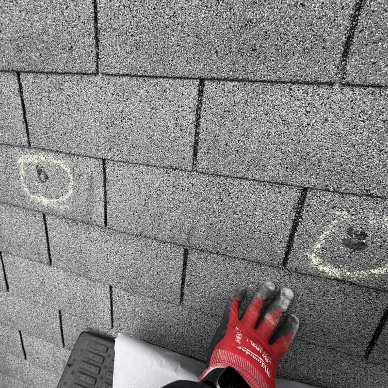 Roof shingles with marked damage spots and gloved hand