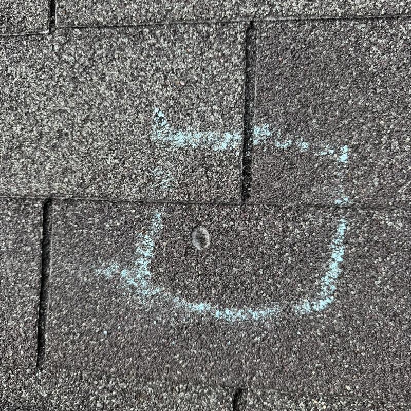 Roof shingles with marked damage spot on asphalt surface