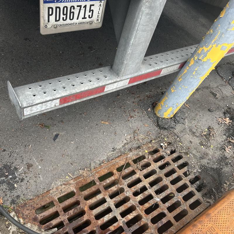Storm drain grate with nearby trailer and pole