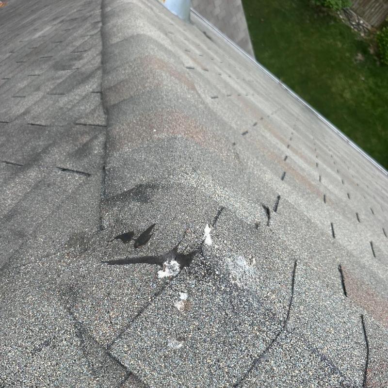 Asphalt roof shingles with visible damage near ridge vent