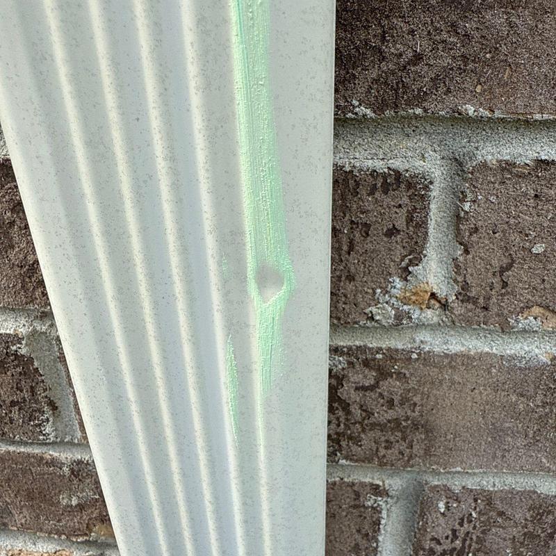 Vinyl siding with hail damage dent near brick wall