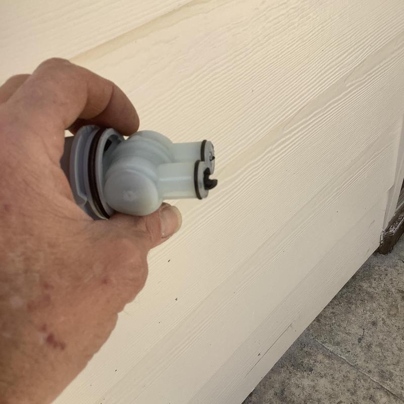 Toilet fill valve part held by hand near exterior wall