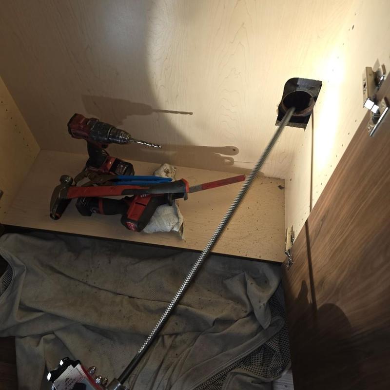 Drain line clog clearing with cable and tools inside cabinet