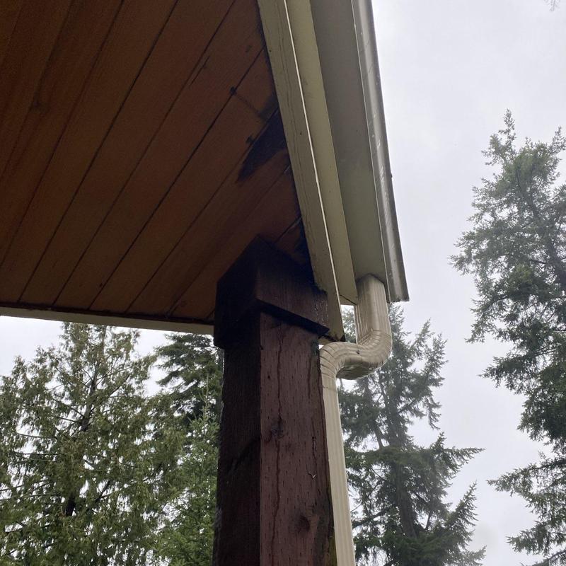 Gutter downspout and wooden support post with water stains