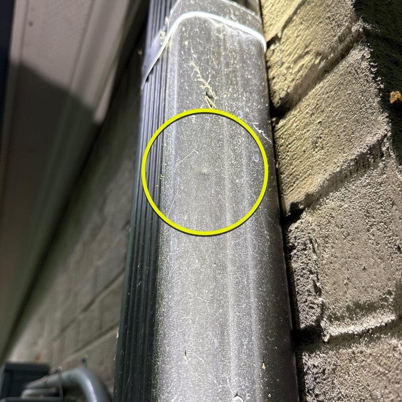 Metal downspout with dent and debris near brick wall