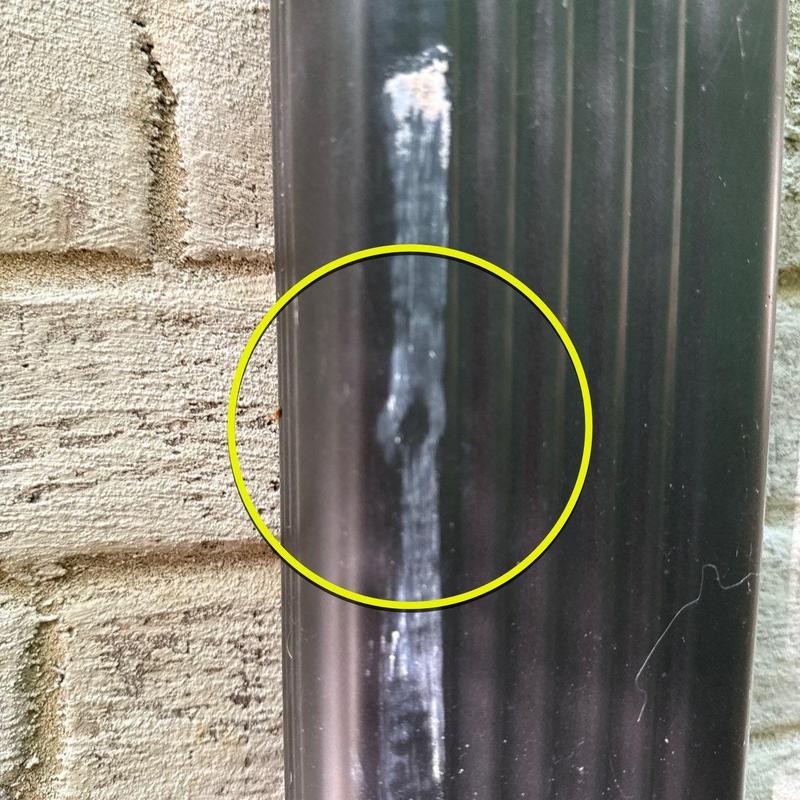 Downspout dent damage circled on black metal pipe