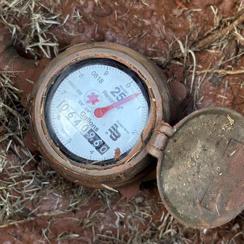 Water meter dial with rusted cover in soil pit