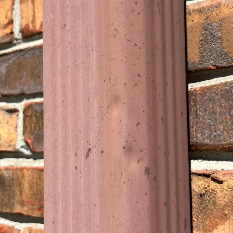 Vinyl downspout with hail damage dents on brick wall