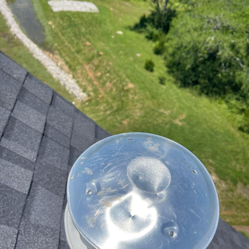 Metal ridge vent cap with hail damage on asphalt roof