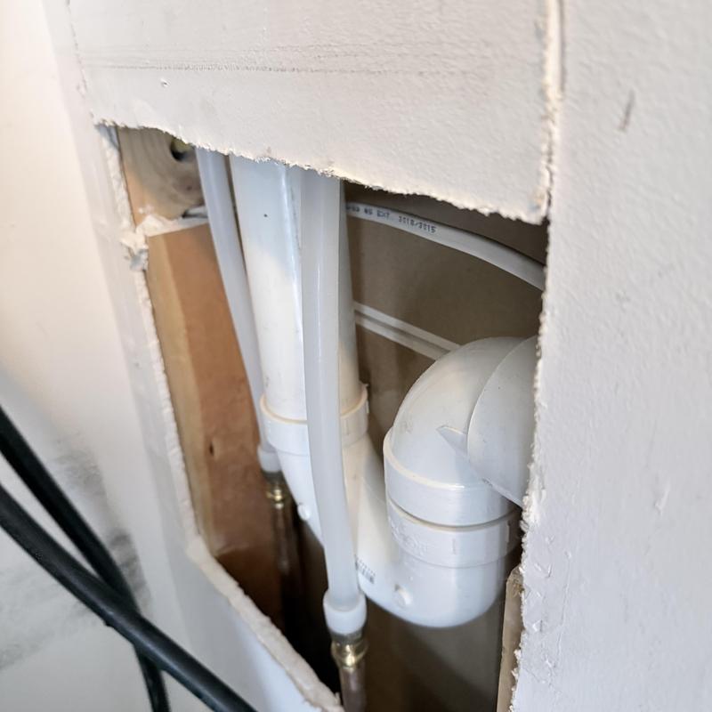 Laundry valve and PVC drain pipe behind wall panel