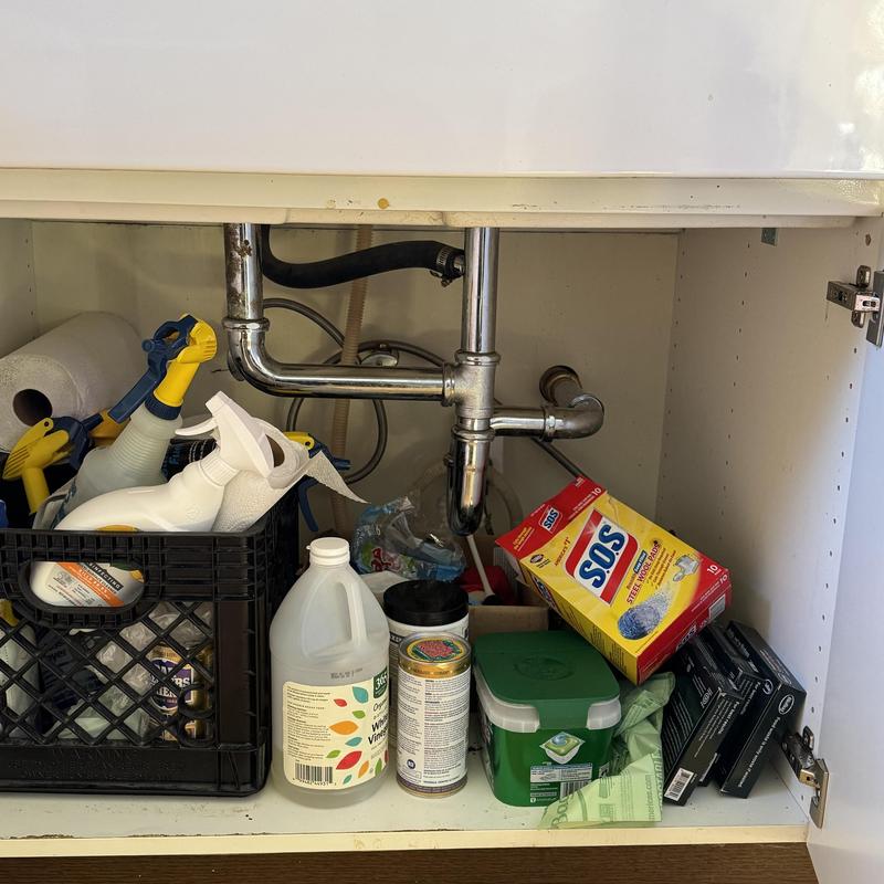 Kitchen sink drain pipes with cleaning supplies stored below