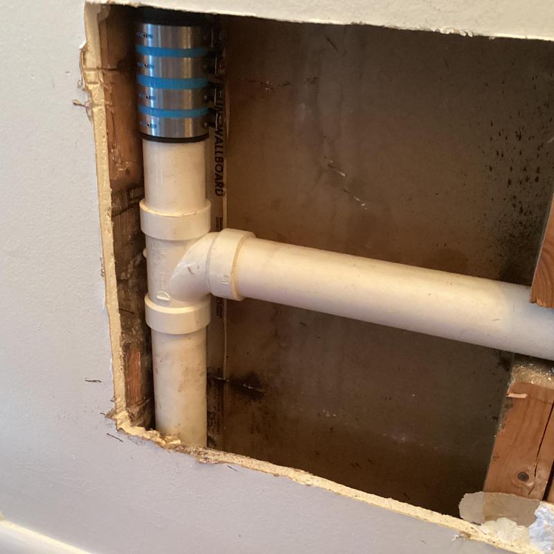 PVC drain pipe with metal riser clamp behind drywall