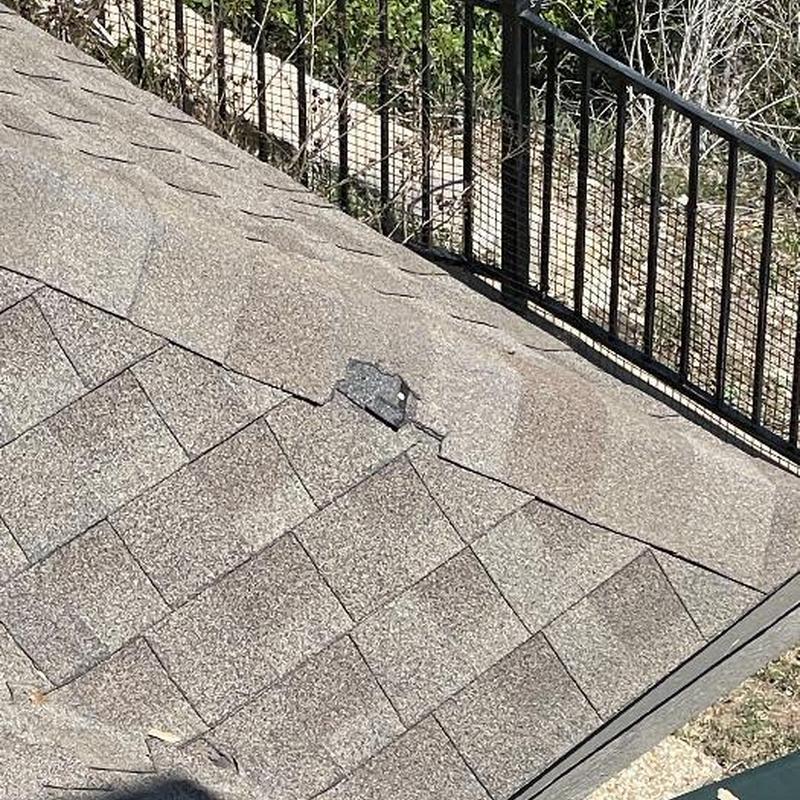 Asphalt roof shingles with visible damage near fence