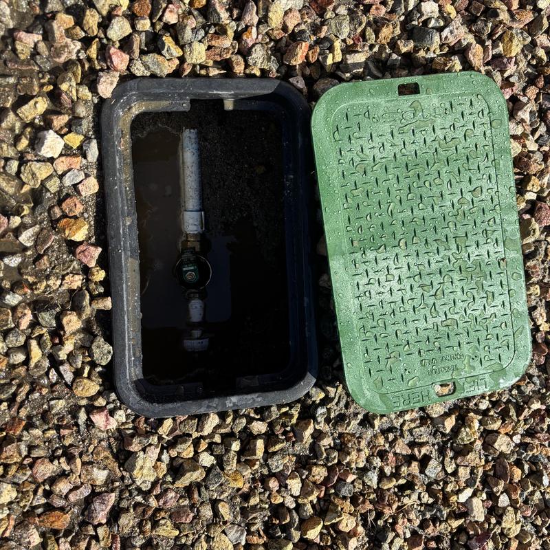 Water meter box with broken water main in gravel ground