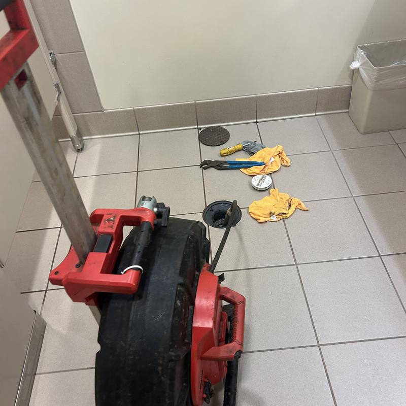 Main line drain with plumber’s snake and tools on tile floor Main line drain with plumber’s snake and tools on tile floor