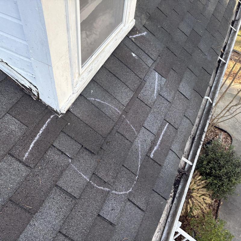 Asphalt roof shingles with marked damage near dormer window