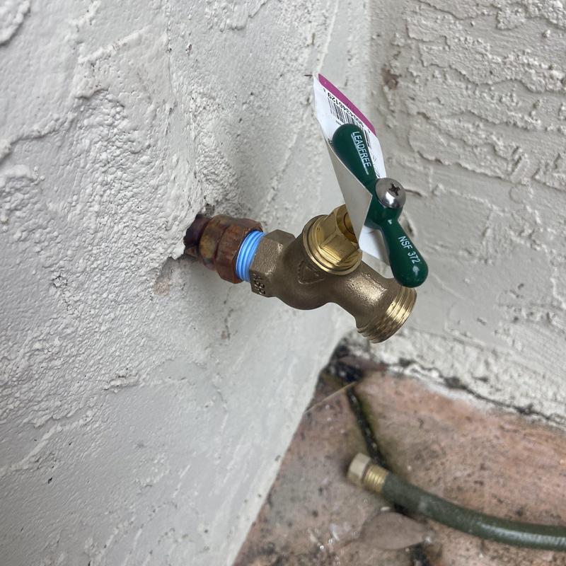 Hose bib valve with green handle on exterior wall