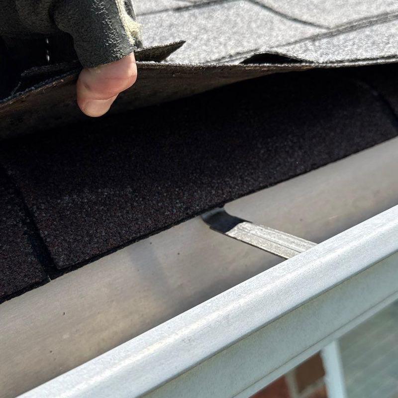 Asphalt roof shingles lifted showing underlying gutter system