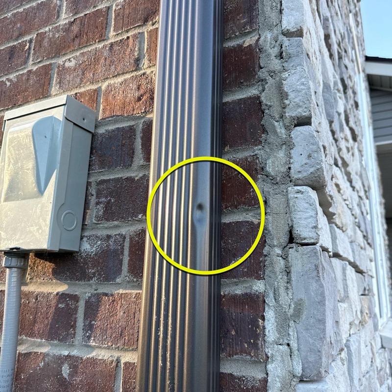 Downspout dent on exterior brick wall near utility box