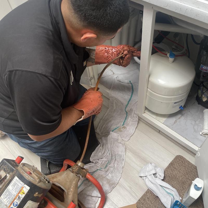 Kitchen sink drain snake clearing blockage under cabinet